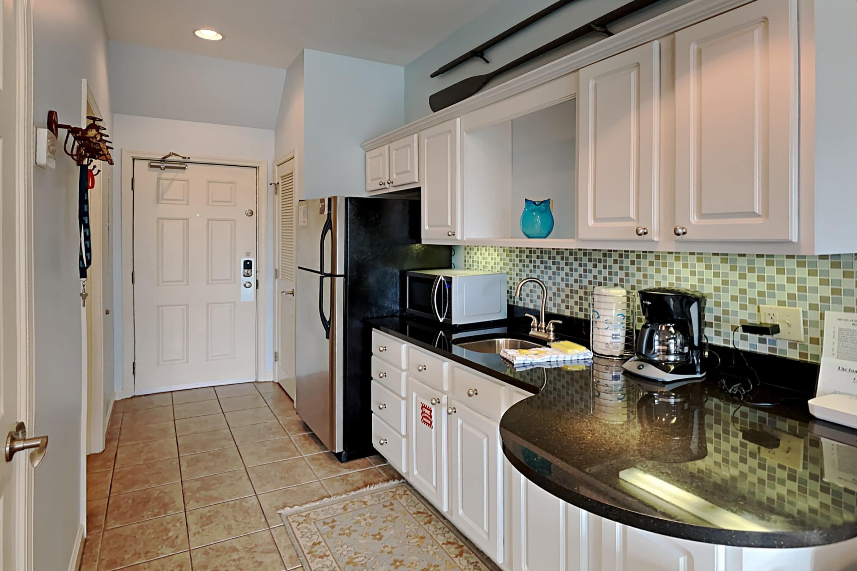 A kitchen with white cabinets, a black refrigerator, a microwave, and a coffee maker.