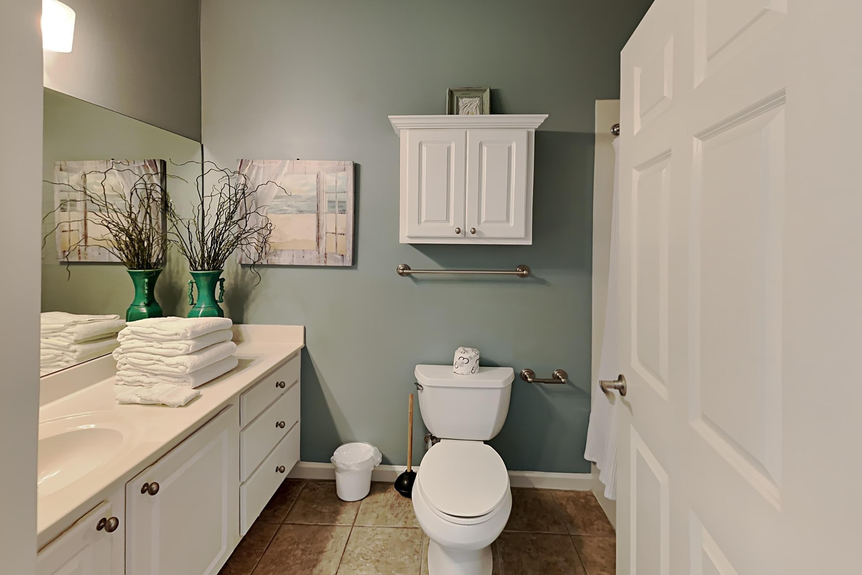A bathroom with a white toilet, a sink, and a cabinet. There are two green vases on the counter.