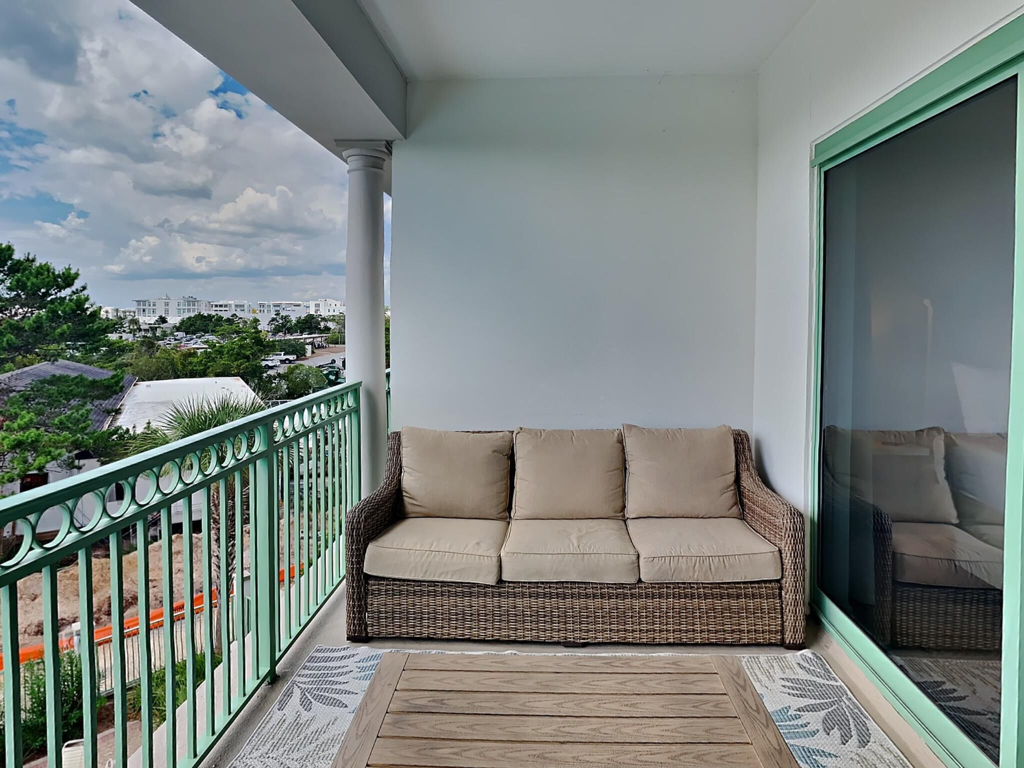 A balcony with a wicker sofa and a view of buildings and trees.