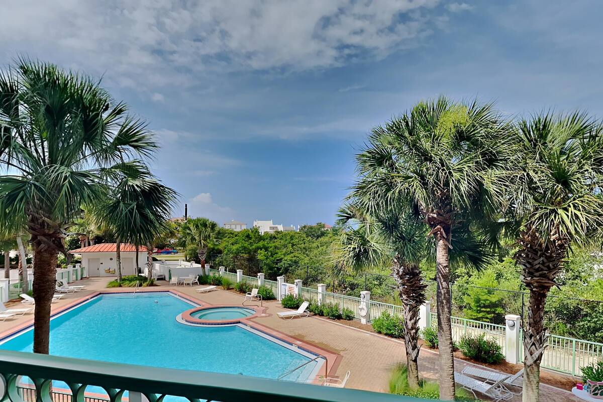 A swimming pool surrounded by palm trees and lounge chairs, with a view of buildings in the background.