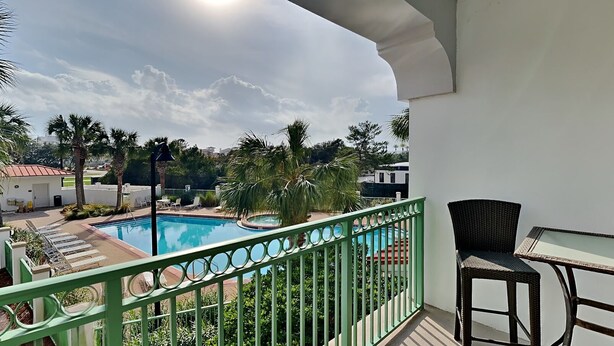 Un balcon avec vue sur une piscine, des chaises longues et une table.