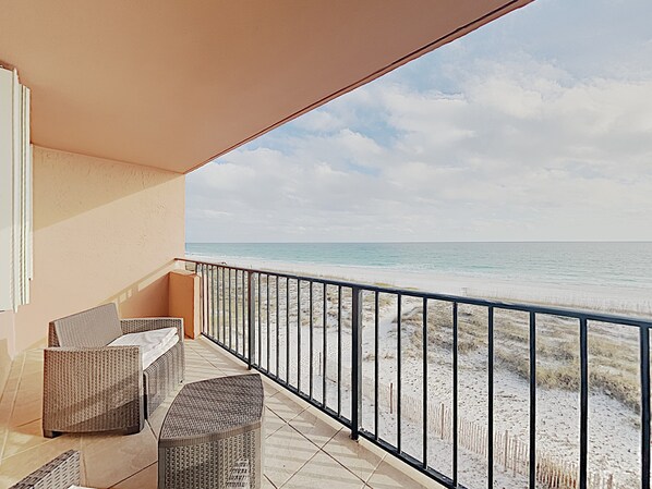 A balcony with wicker furniture overlooking a beach.