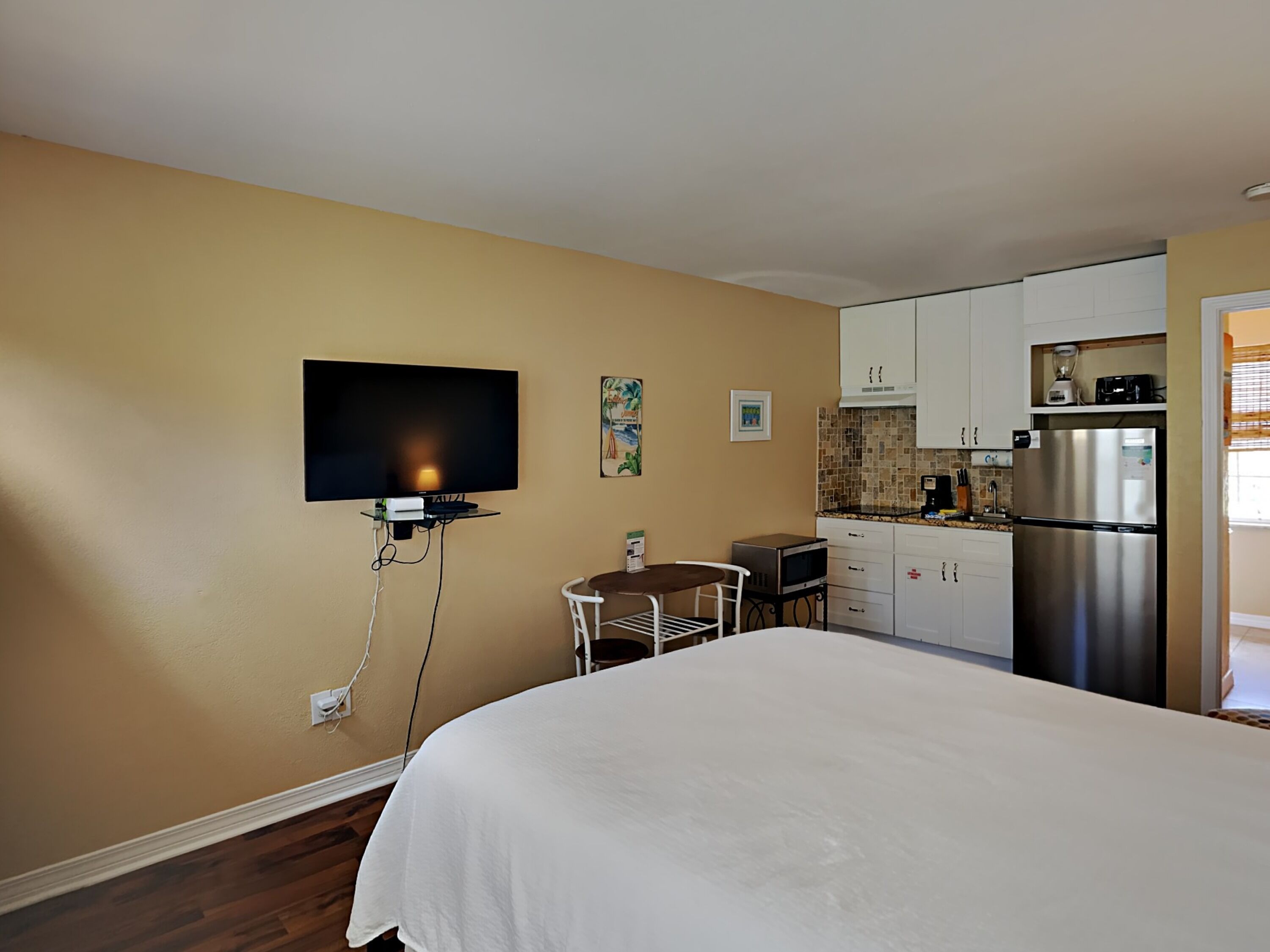 Hotelkamer met een bed, een aan de muur bevestigde televisie, een kleine eettafel en een kitchenette met een koelkast en magnetron.