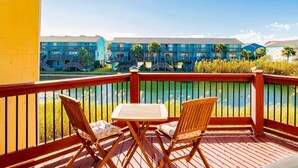 A wooden deck with two chairs and a table, overlooking a body of water and a row of blue buildings.