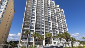 Un hotel di grandi dimensioni con numerosi balconi, un design architettonico moderno e palme sullo sfondo.