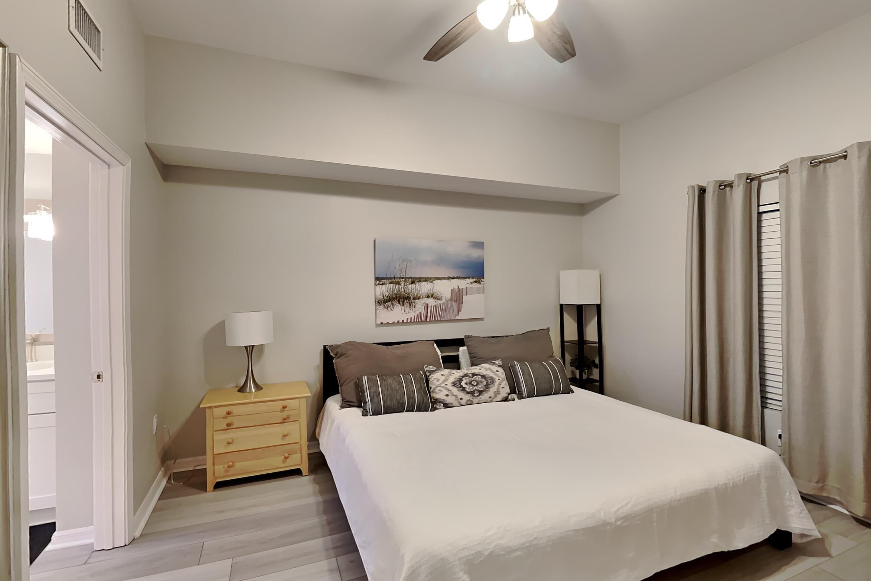 Un dormitorio con cama, mesitas de noche, un ventilador de techo y un cuadro en la pared.