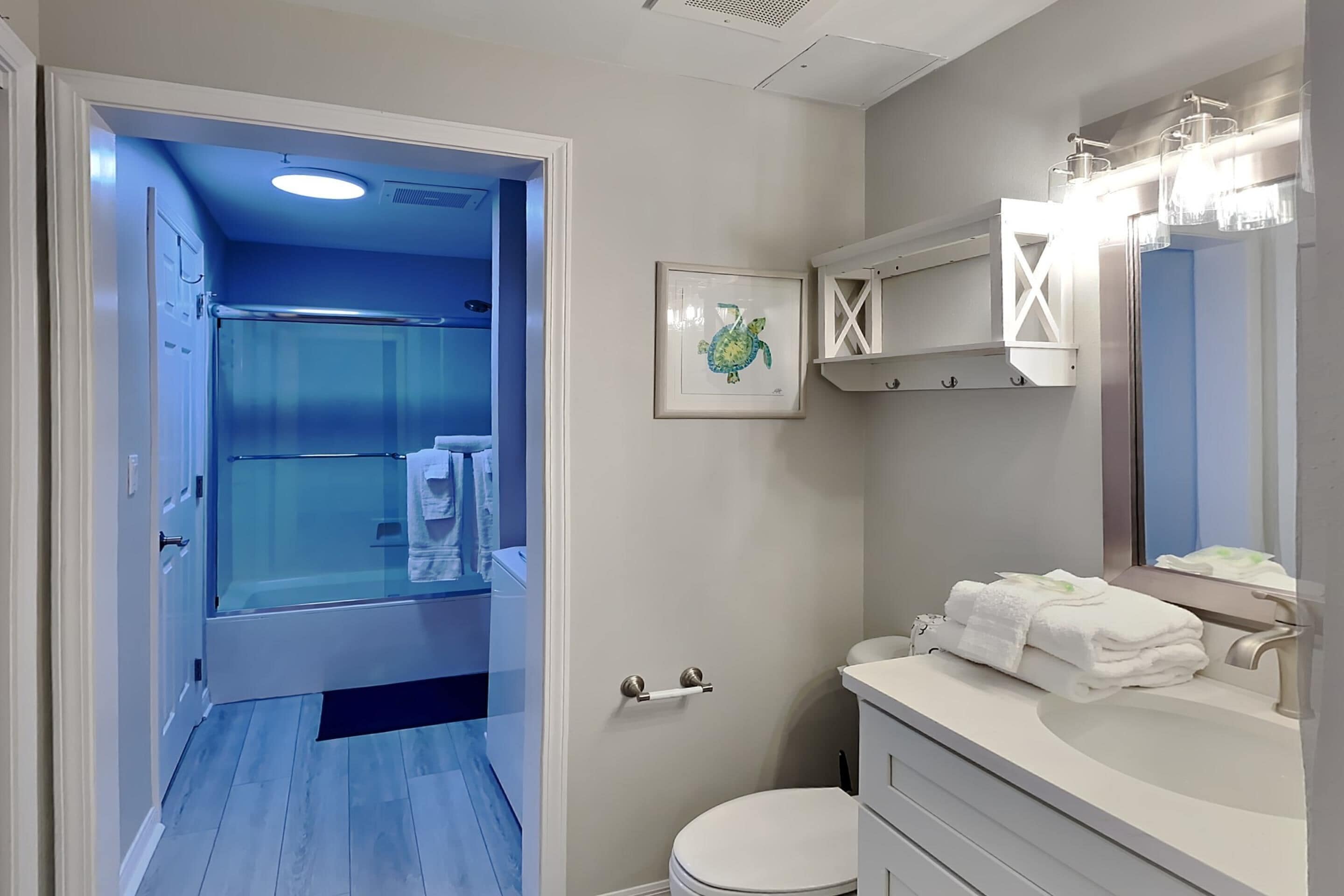A bathroom with a glass shower enclosure, a white sink with a mirror, and a framed picture on the wall.