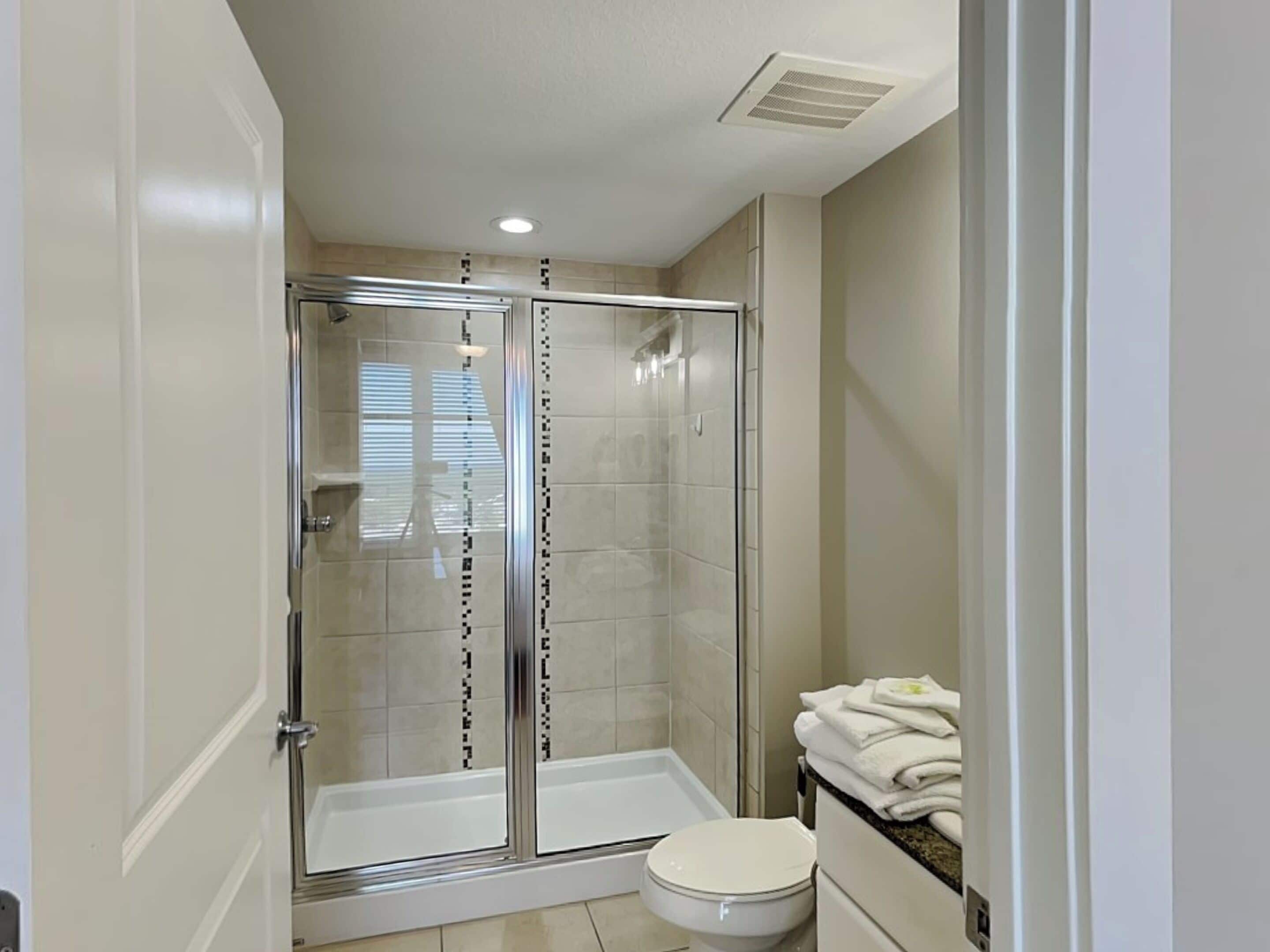 A modern bathroom with a glass-enclosed shower, a toilet, and a sink with a towel rack.
