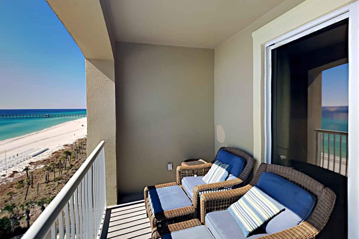 A balcony with wicker furniture, a view of the beach, and a clear sky.