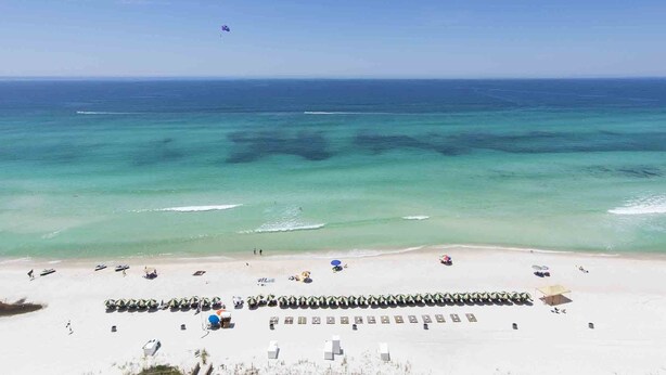 Una playa con agua turquesa cristalina, una hilera de sombrillas y algunas personas.