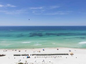 A beach with clear turquoise water, a row of beach umbrellas, and a few people.