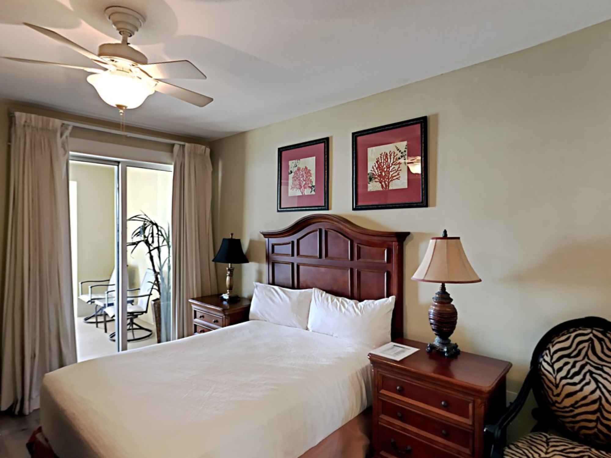 A hotel room with a bed, a nightstand, a lamp, a chair, and a ceiling fan.