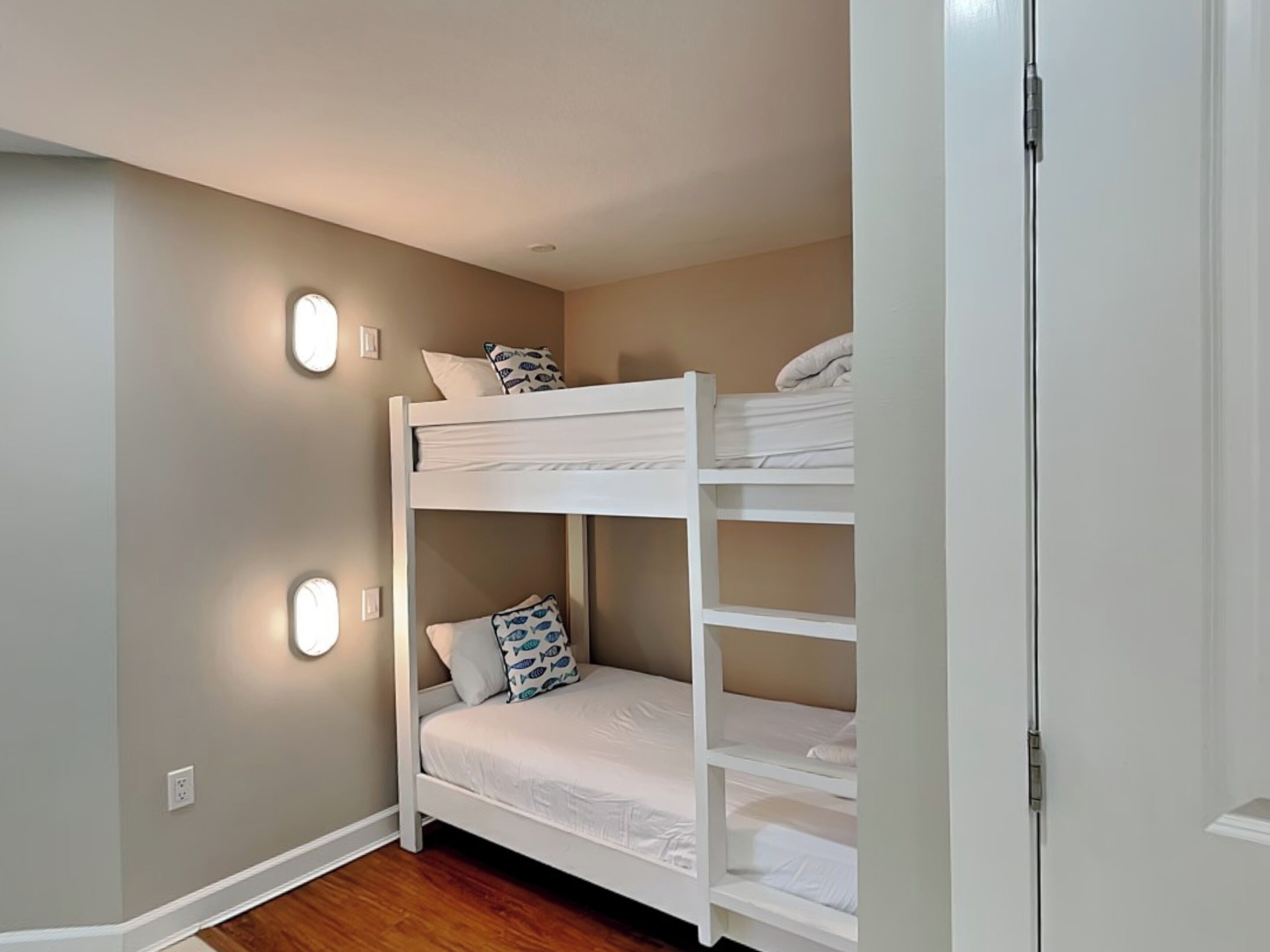 A bunk bed room with two beds, each with pillows and a blanket. There are wall-mounted lights on either side of the beds.