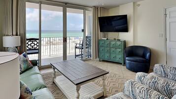 Una habitación con sofá, una mesa de centro, un televisor en un mueble, un ventilador de techo y vista a la playa.