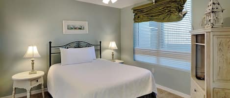 A bedroom with a bed, two bedside tables with lamps, a ceiling fan, a window with blinds, and a dresser.