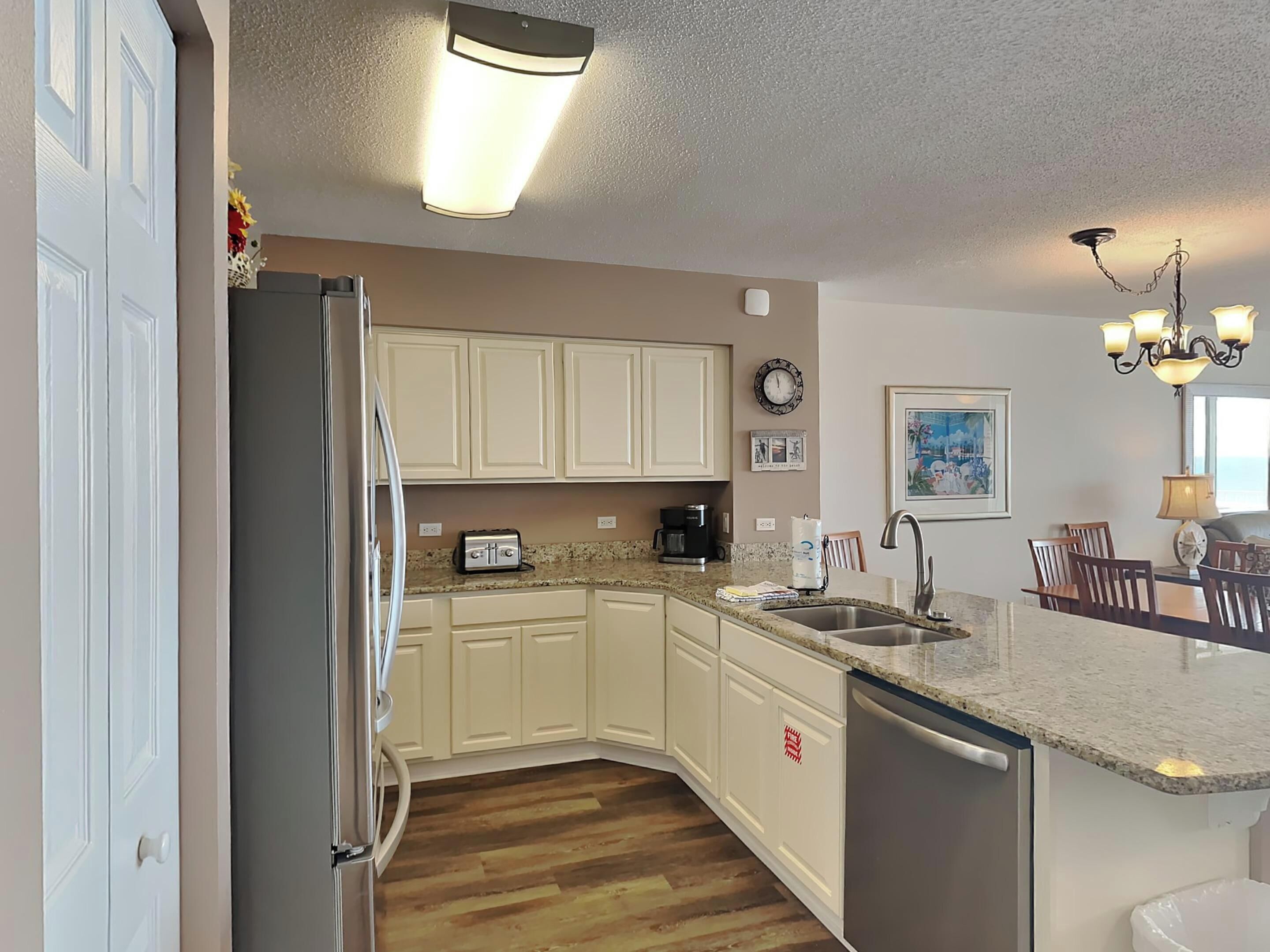 A kitchen with white cabinets, a granite countertop, a stainless steel refrigerator, a coffee maker, and a sink.