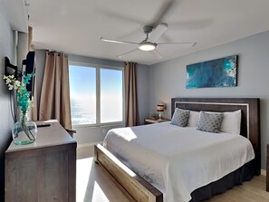 Relax in this serene hotel room with a large bed, nightstand, and ceiling fan, offering a stunning ocean view.