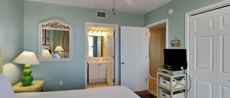 A hotel room with a bed, a ceiling fan, a bathroom with a vanity, and a TV on a stand.