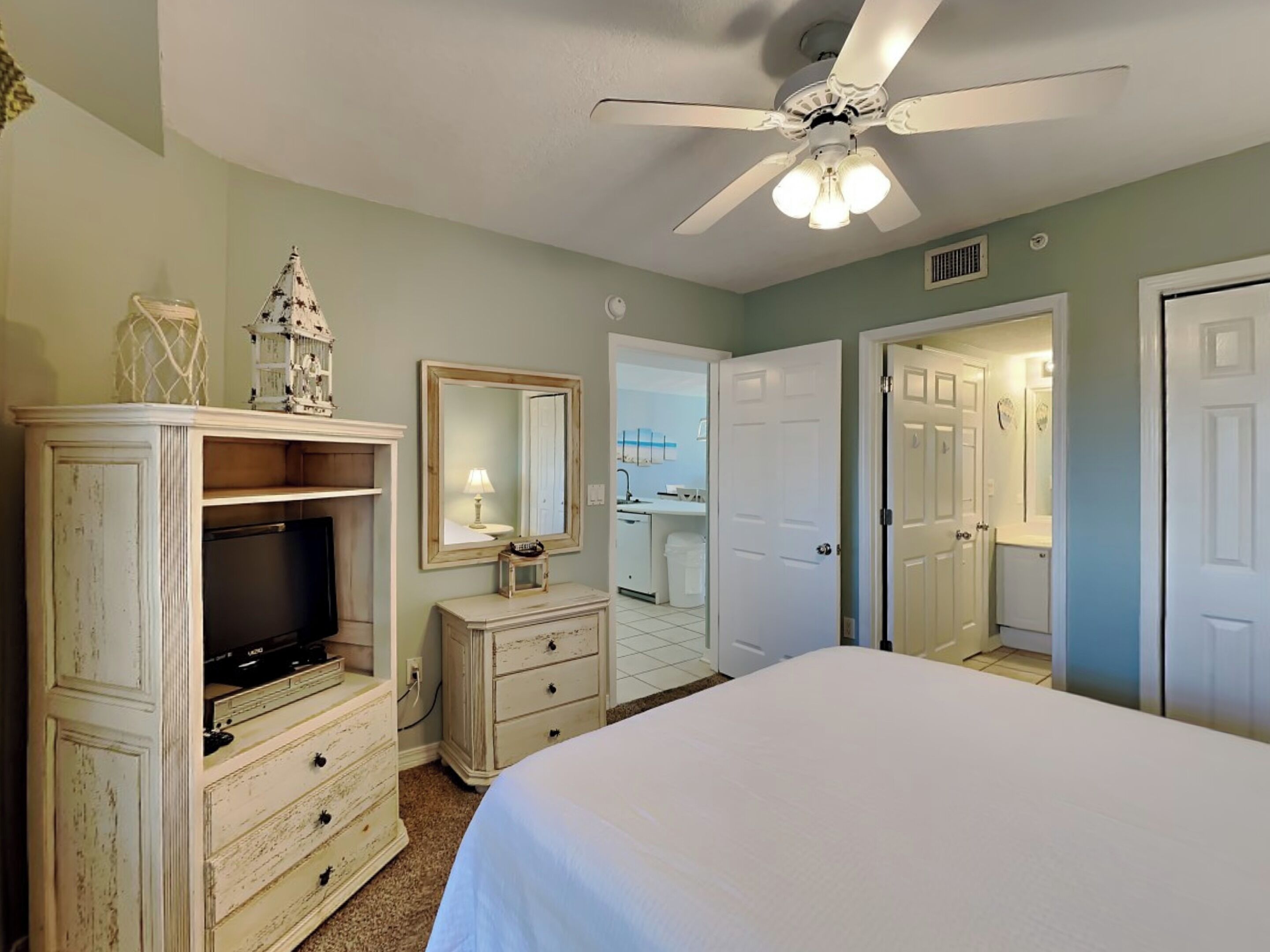 A bedroom with a bed, a dresser, a television, a ceiling fan, and a mirror.