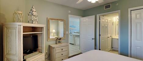 A bedroom with a bed, a dresser, a television, a ceiling fan, and a mirror.