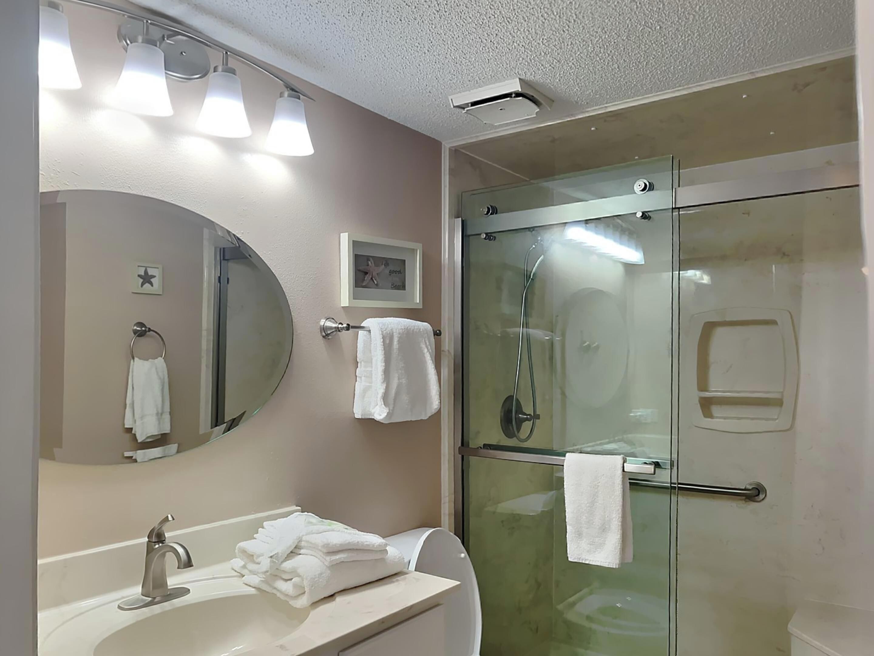 Ein Badezimmer mit einer Duschkabine, einem Waschbecken mit Spiegel und einem gerahmten Bild an der Wand.
