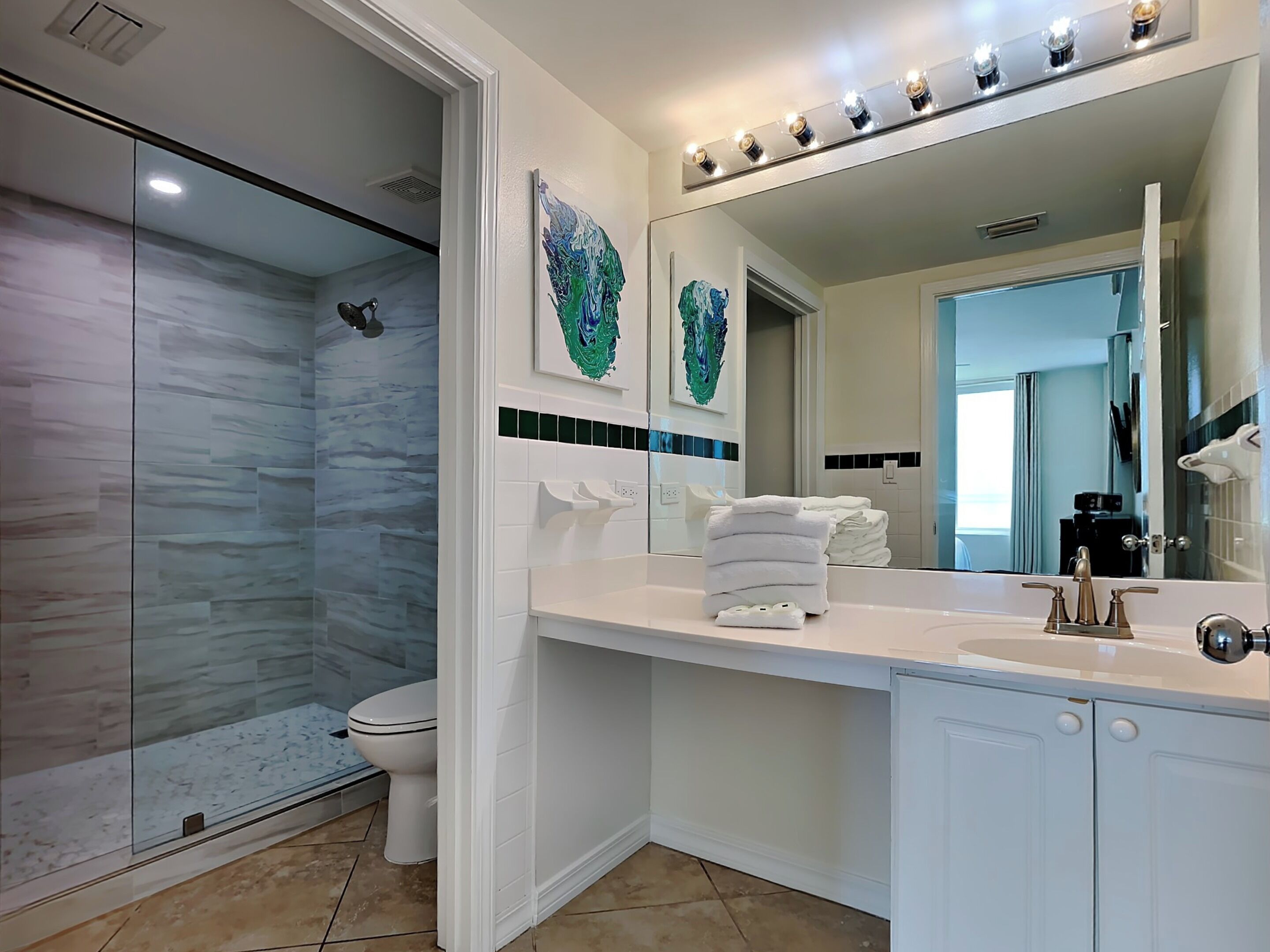 Un baño moderno con cabina de ducha de vidrio, un inodoro blanco, un lavamanos con espejo y una pila de toallas blancas.