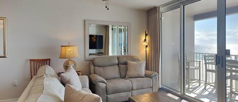 Una sala de estar con ventilador de techo, un sofá, un sillón reclinable, una mesa de centro y un ventanal con vistas al océano.