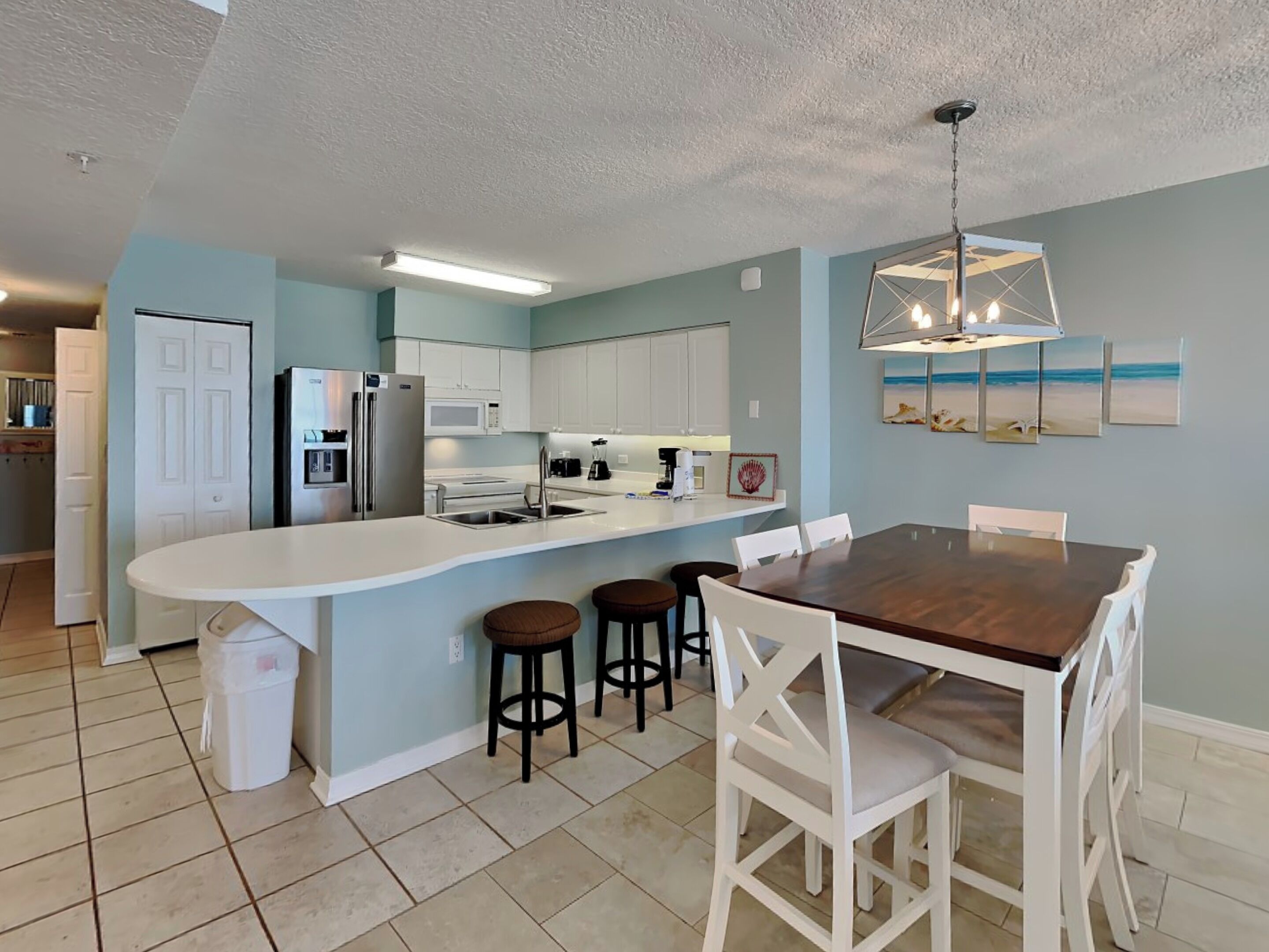 A modern kitchen with white cabinets, a central island with stools, and a dining table with chairs.