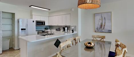 A modern kitchen with white cabinetry, a central island, and a dining area with wooden chairs.