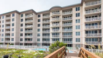Un edificio residencial de varios pisos con balcones, una piscina y un puente de madera que lleva al área de la piscina.