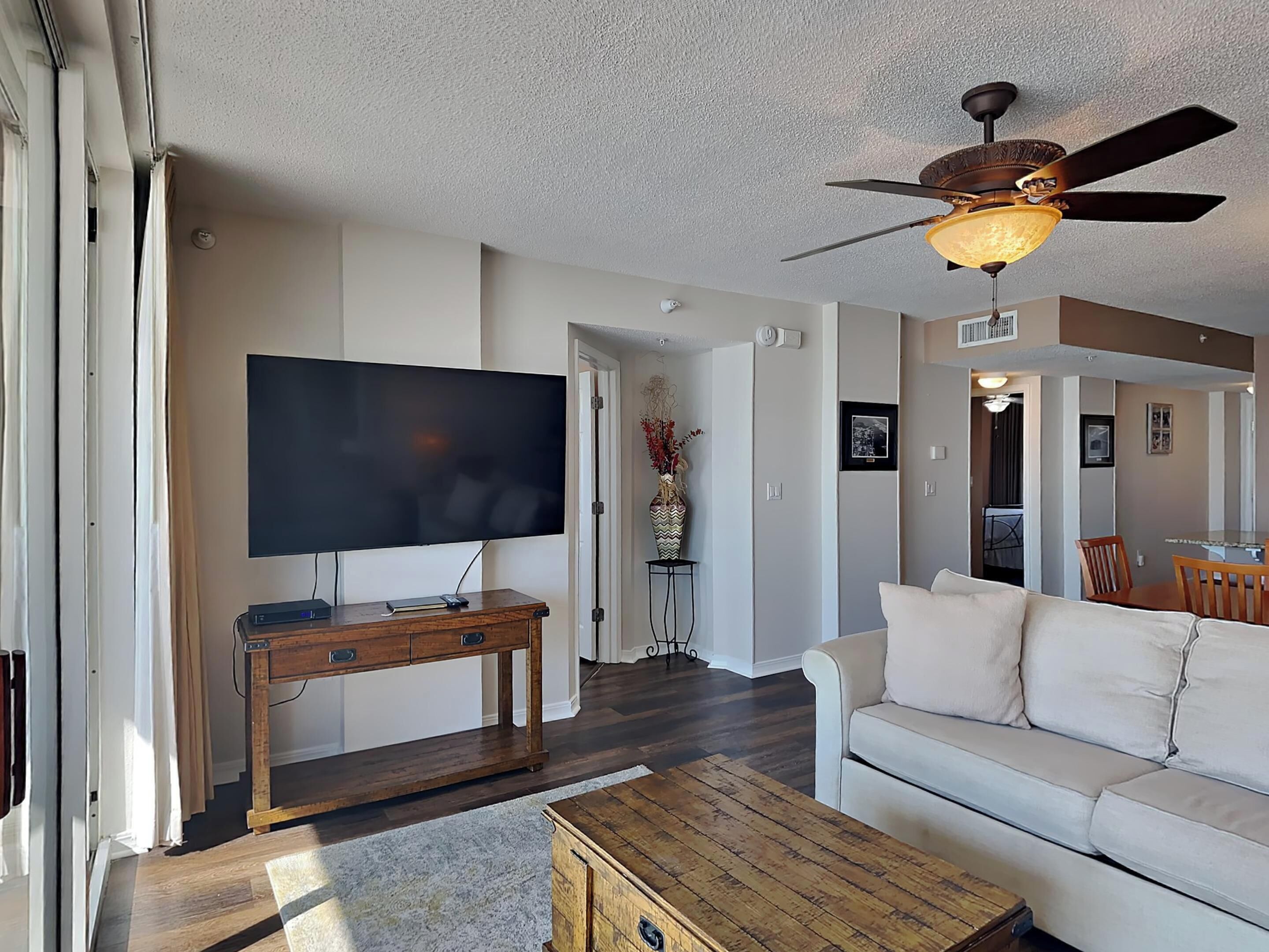 A living room with a flat-screen TV, wooden coffee table, and a ceiling fan.