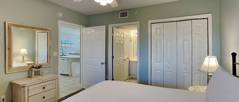 A bedroom with a large bed, a ceiling fan, a dresser, a mirror, and two doors leading to other rooms.