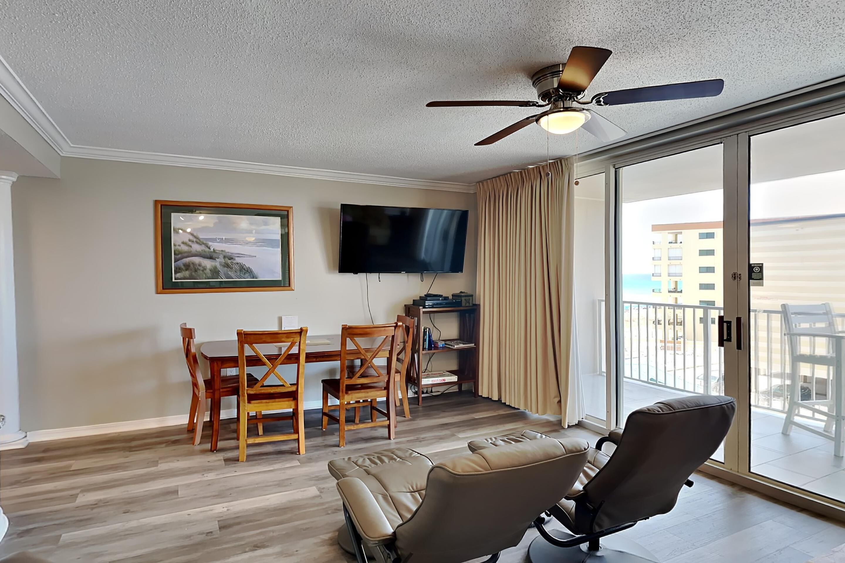 A living room with a dining area, a TV, and a balcony with a view.