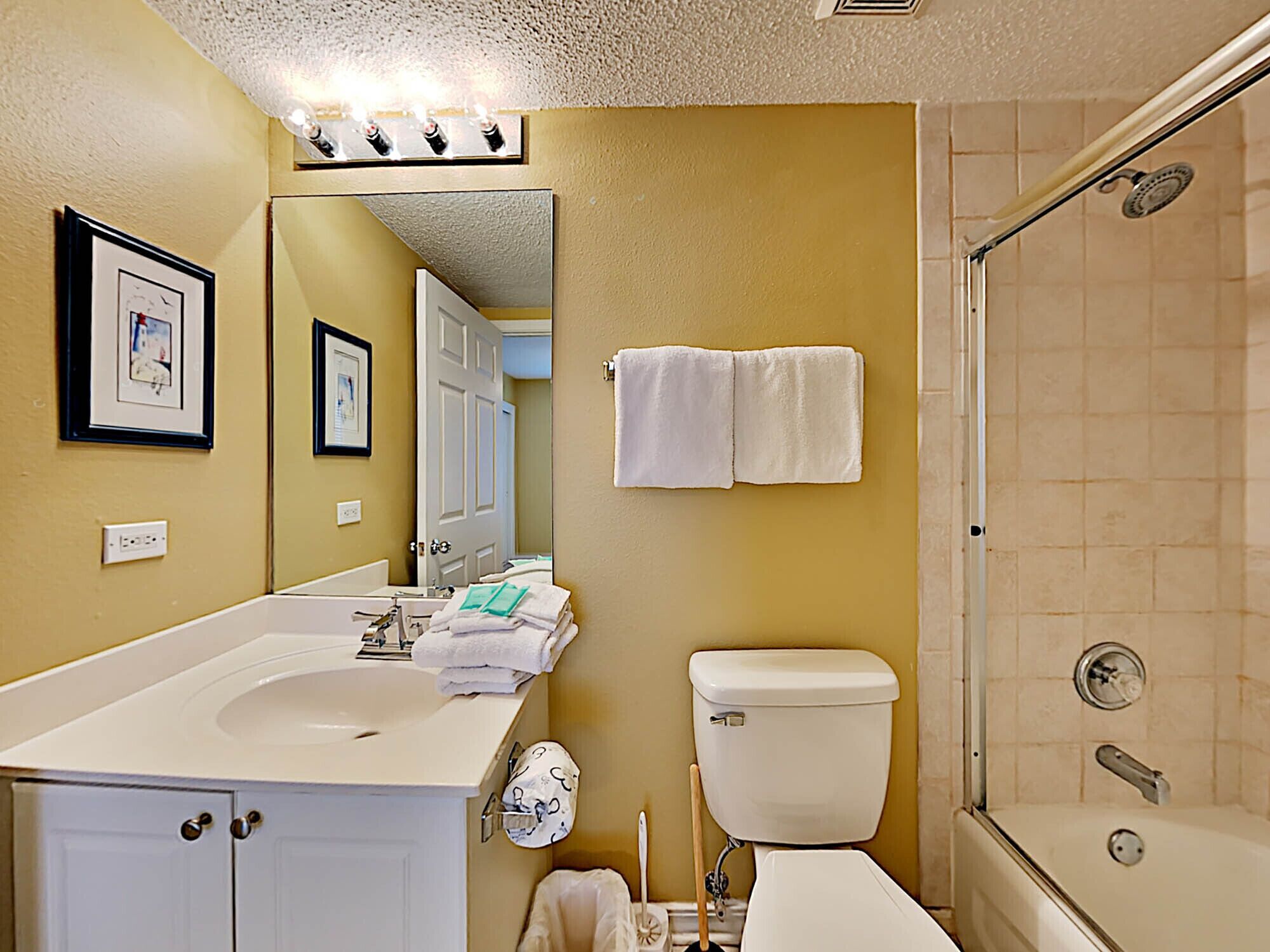 A bathroom with a sink, toilet, and shower. There are towels hanging on the wall and a mirror above the sink.