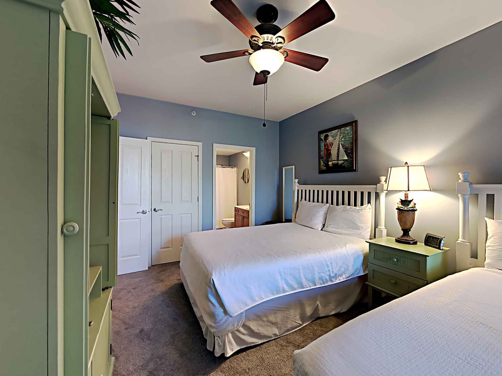 A bedroom with a bed, a nightstand, a lamp, a ceiling fan, and a painting on the wall.