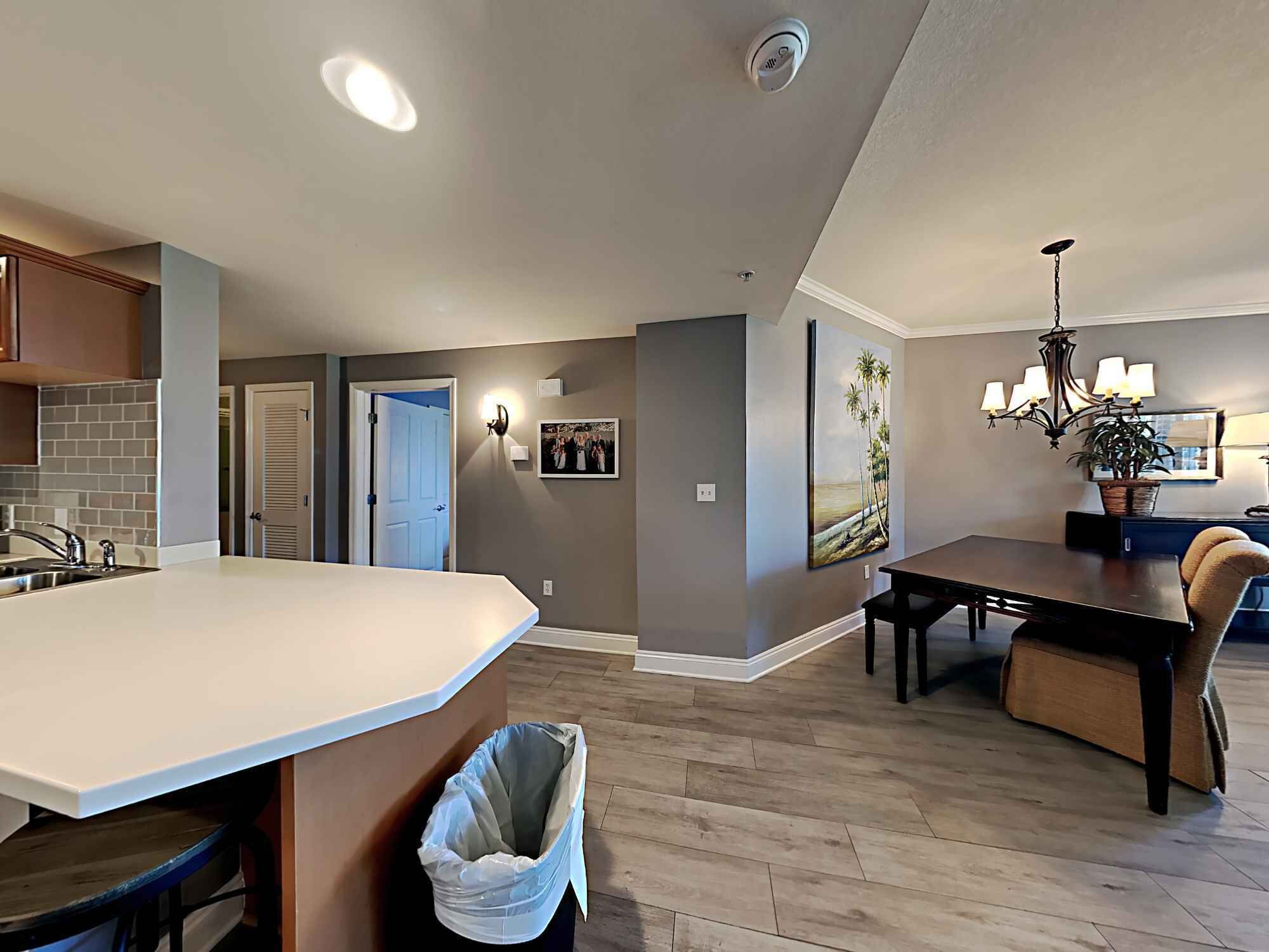 A modern kitchen with a large island, a dining area with a chandelier, and a hallway leading to bedrooms.
