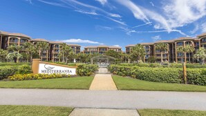 A hotel with a Mediterranean theme, featuring a central pathway, palm trees, and a clear blue sky. - Mediterranea by Southern Vacation Rentals (Miramar Beach)