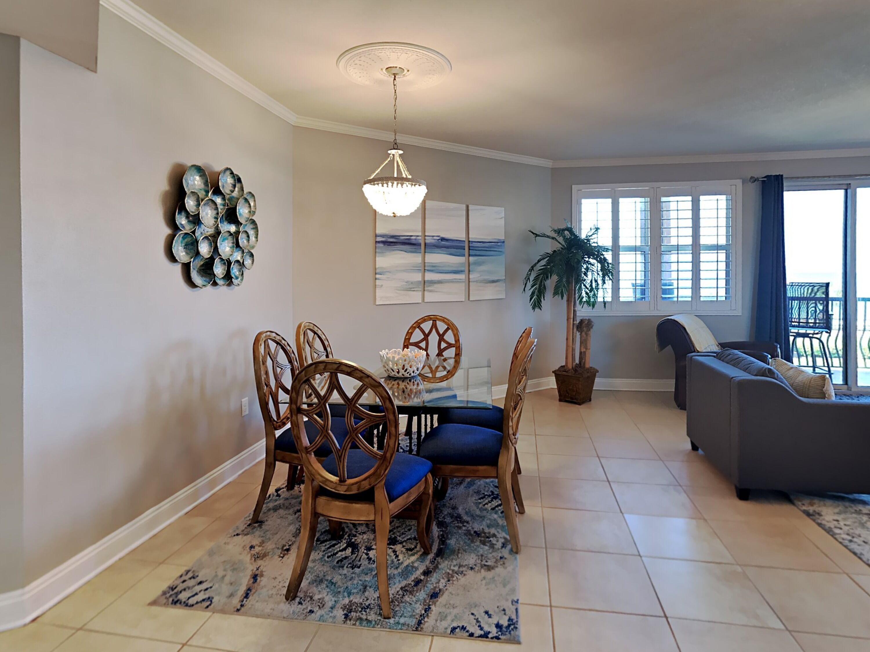 A dining area with a chandelier, a dining table with chairs, and a large potted plant.