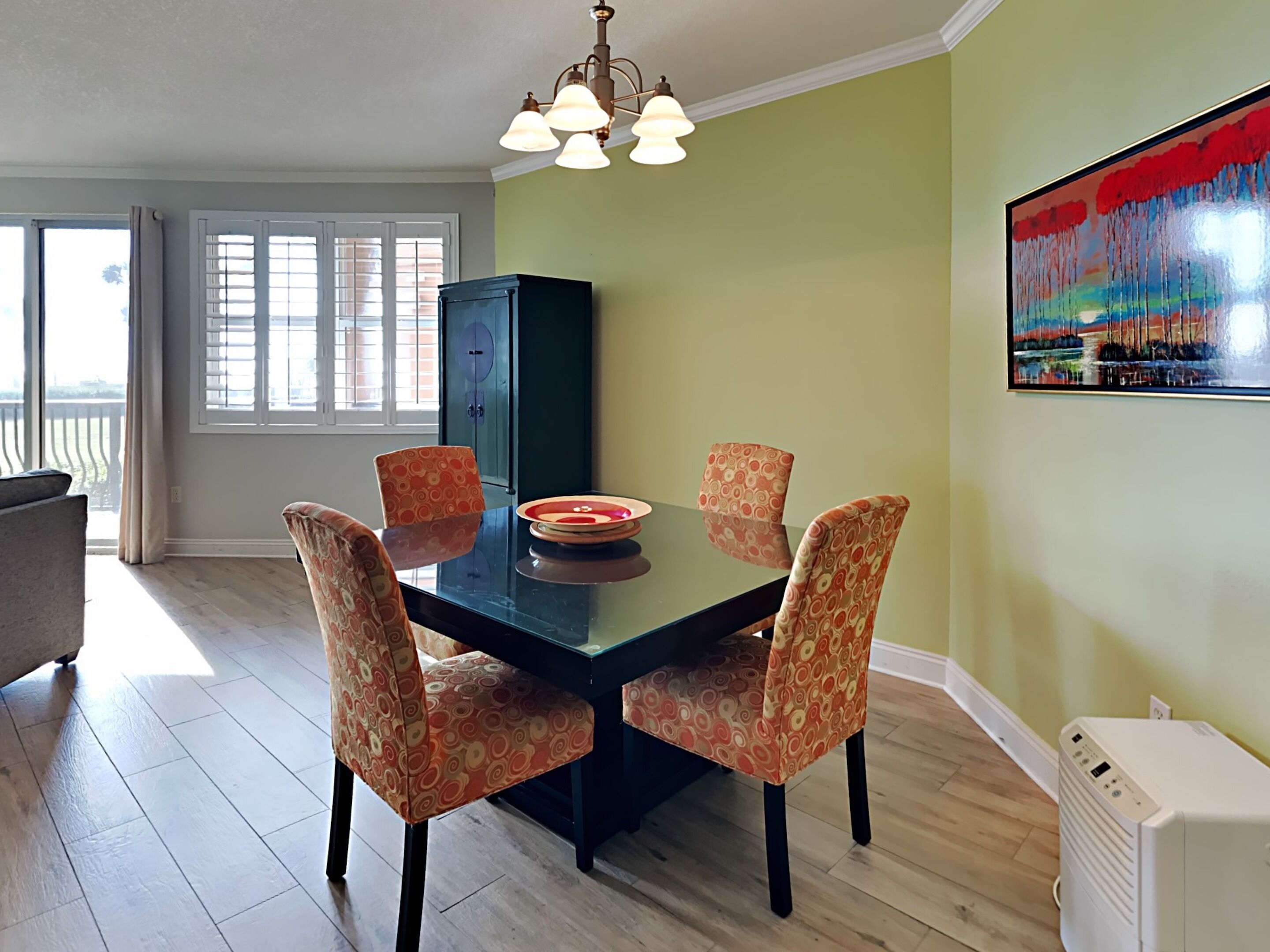 Un coin repas avec une table en verre, quatre chaises à motifs, un buffet et un tableau accroché au mur.