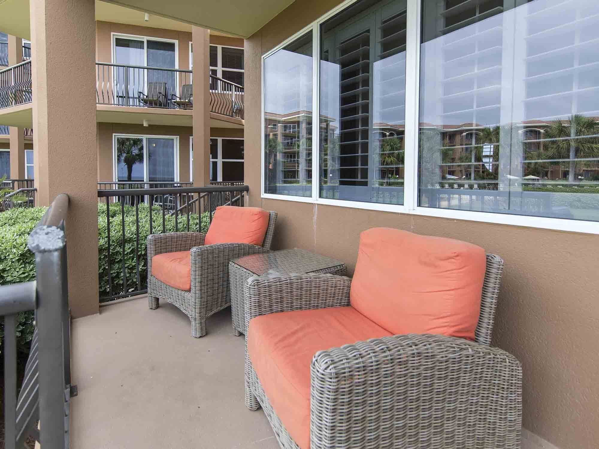 Varanda com móveis de vime e almofadas laranja, com vista para uma área residencial.