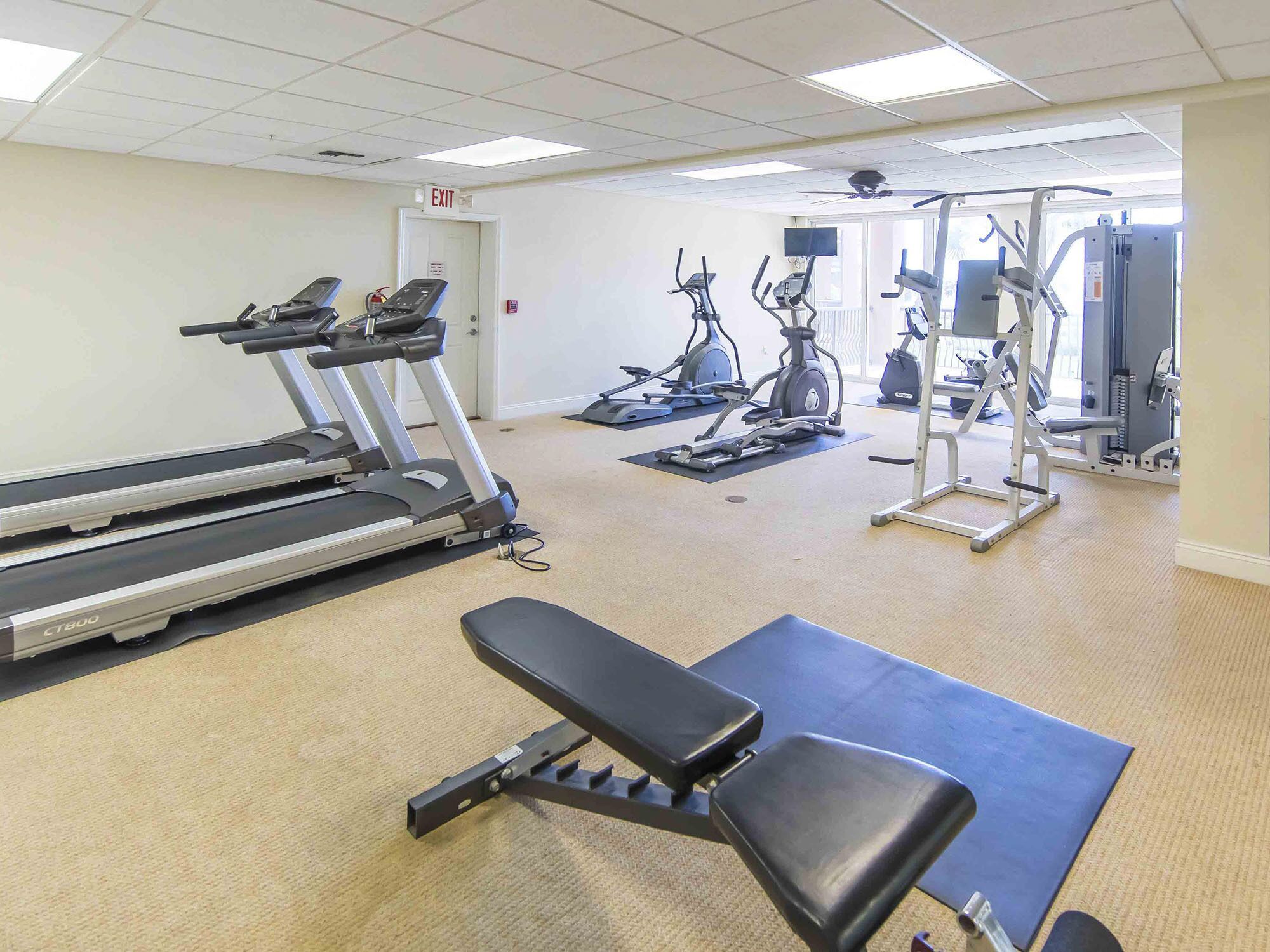 Een sportschool met loopbanden, elliptische trainers en een bank.