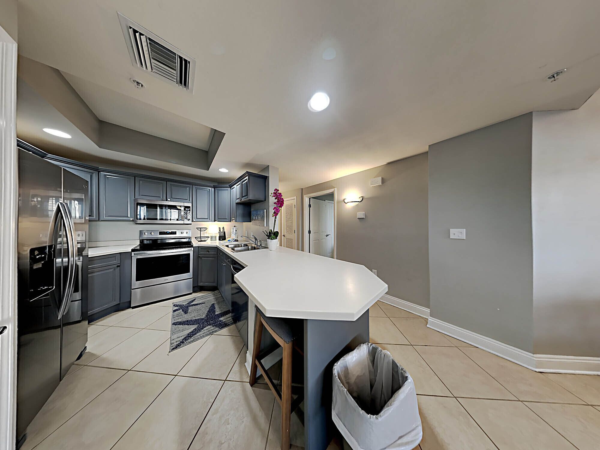 A modern kitchen with grey cabinets, stainless steel appliances, and a white countertop.
