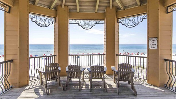 A covered deck with wooden chairs and a view of the beach. - Mediterranea by Southern Vacation Rentals (Miramar Beach)