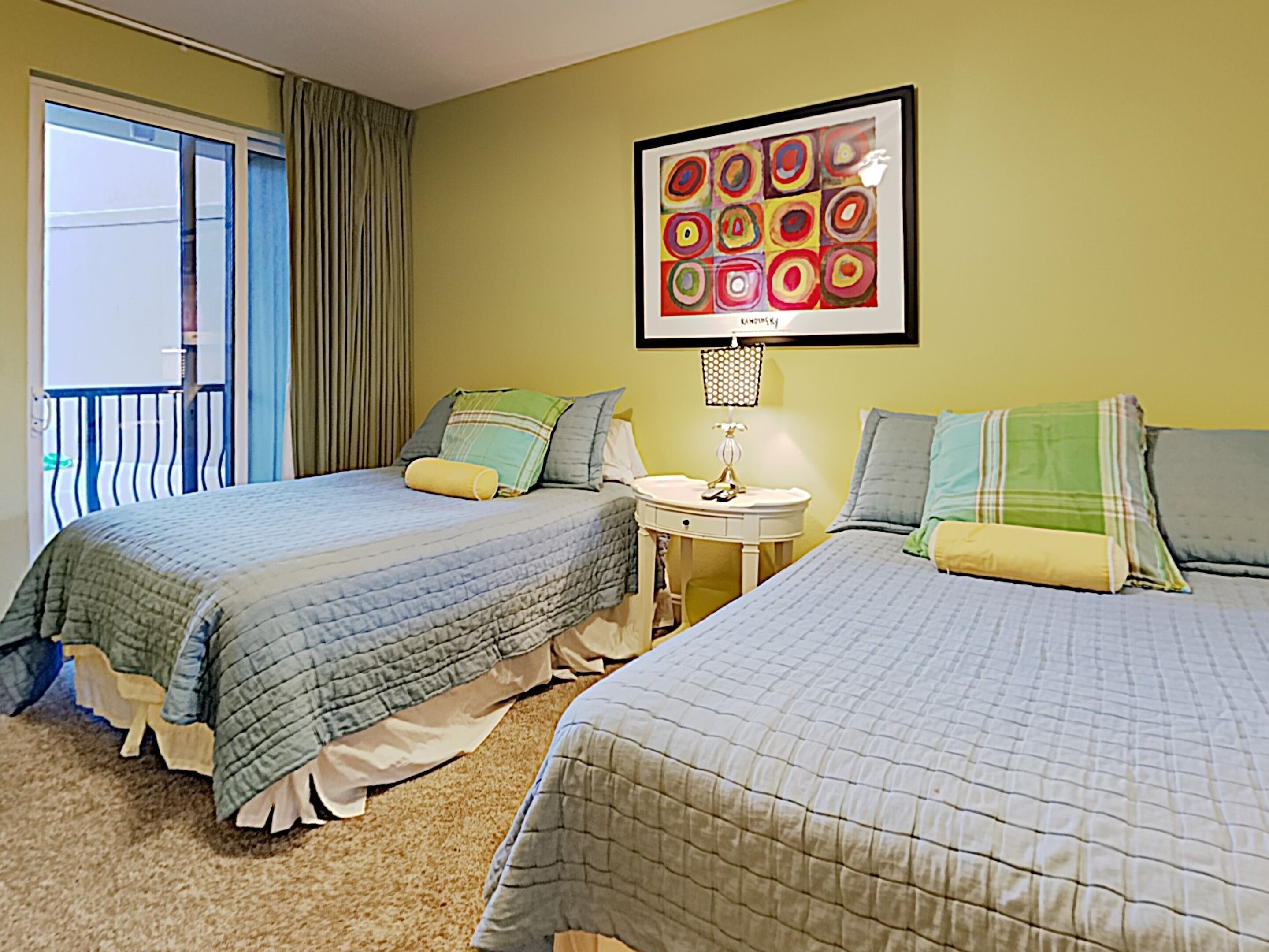 A hotel room with two beds, a small round table, a lamp, and a large abstract painting on the wall.