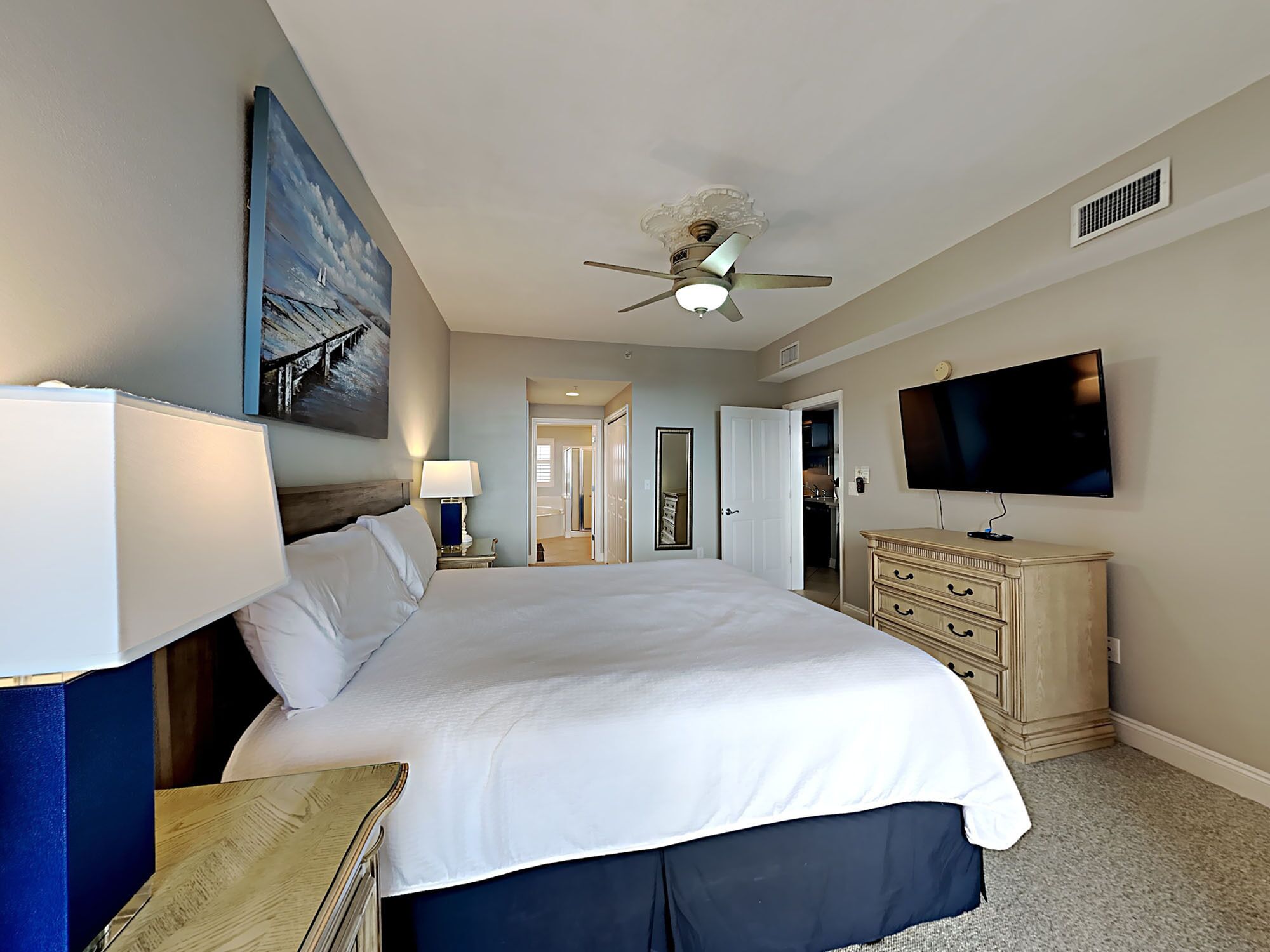 A hotel room with a large bed, a ceiling fan, a television, and a dresser.