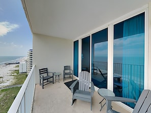 Enjoy the unobstructed ocean view from this balcony, featuring two comfortable chairs and a small table.