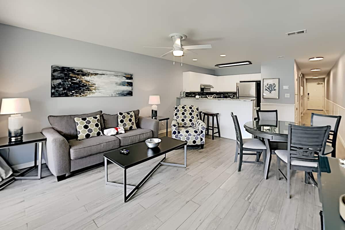 A modern living room with a grey sofa, a coffee table, and a dining area with a glass table and chairs.