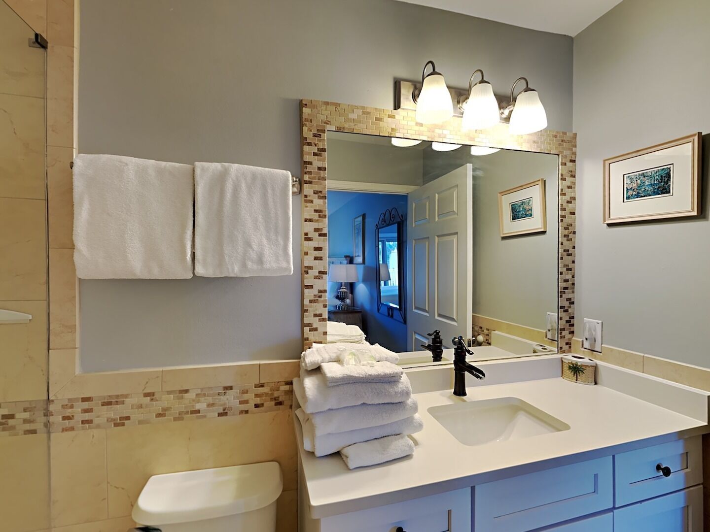 A bathroom with a white sink, a large mirror with a mosaic frame, and a stack of white towels.