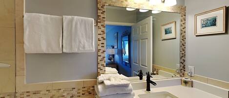 A bathroom with a white sink, a large mirror with a mosaic frame, and a stack of white towels.