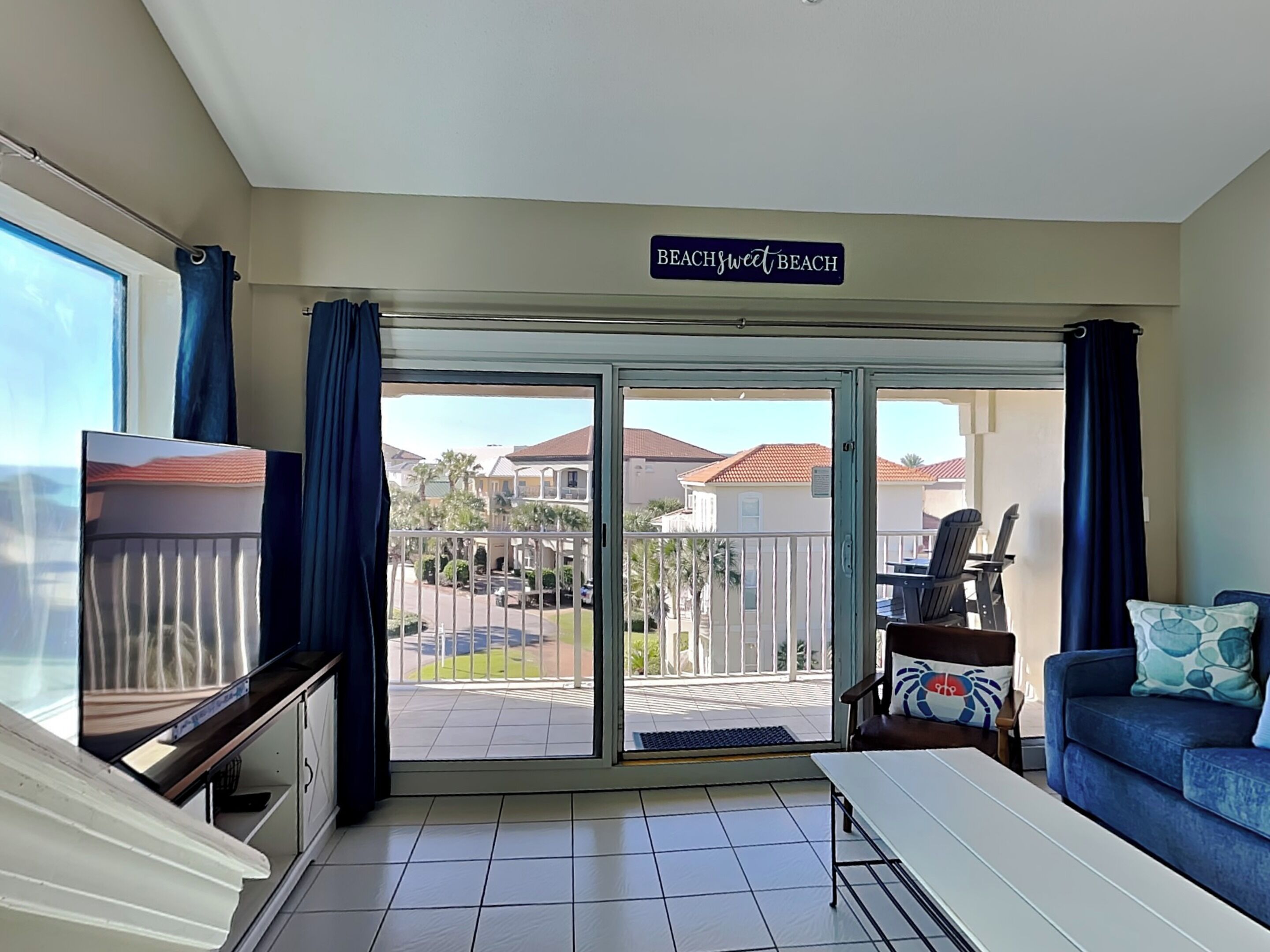 A room with a sliding glass door leading to a balcony, a TV, a sofa, and a dining table.